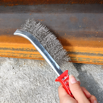 Une brosse métallique en acier inoxydable dans la main d'un homme qui la tient par la poignée rouge