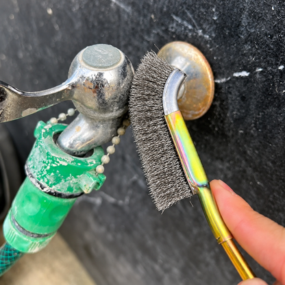 Brosse métallique dans la main d'une personne la tenant devant un robinet