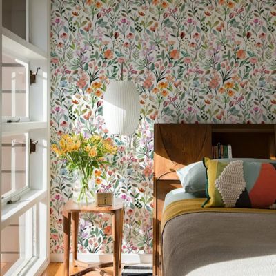 Papier peint fleuri Enchanteur sur un mur derrière un lit